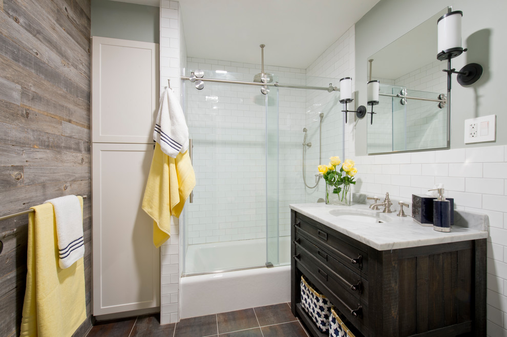Industrial 3/4 bathroom in New York with raised-panel cabinets, white cabinets, a drop-in tub, a shower/bathtub combo, a two-piece toilet, white tile, subway tile, white walls, ceramic floors, a drop-in sink, marble benchtops, a sliding shower screen, brown floor and grey benchtops.