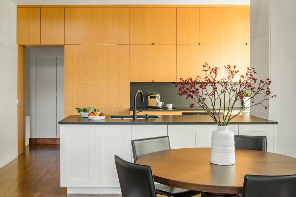 Design ideas for a small transitional galley eat-in kitchen in Boston with a single-bowl sink, flat-panel cabinets, light wood cabinets, soapstone benchtops, black splashback, black appliances, medium hardwood floors and brown floor.