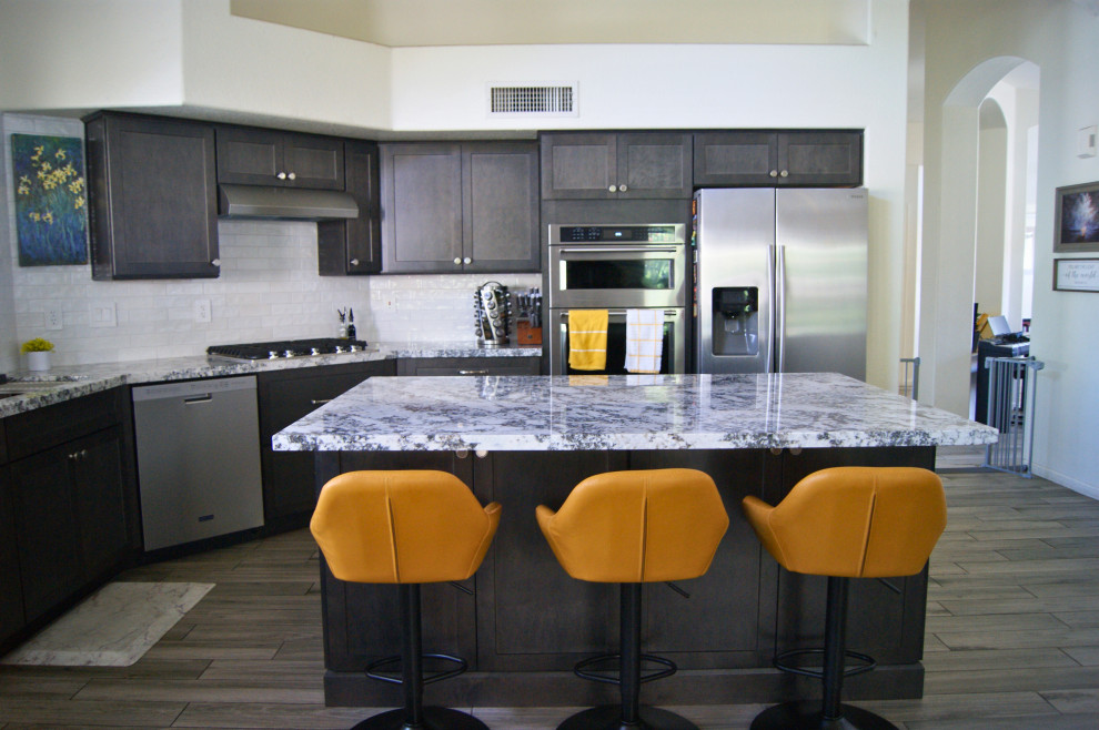Open concept kitchen - mid-sized modern l-shaped porcelain tile and gray floor open concept kitchen idea in Phoenix with an undermount sink, shaker cabinets, brown cabinets, granite countertops, white backsplash, subway tile backsplash, stainless steel appliances, an island and white countertops