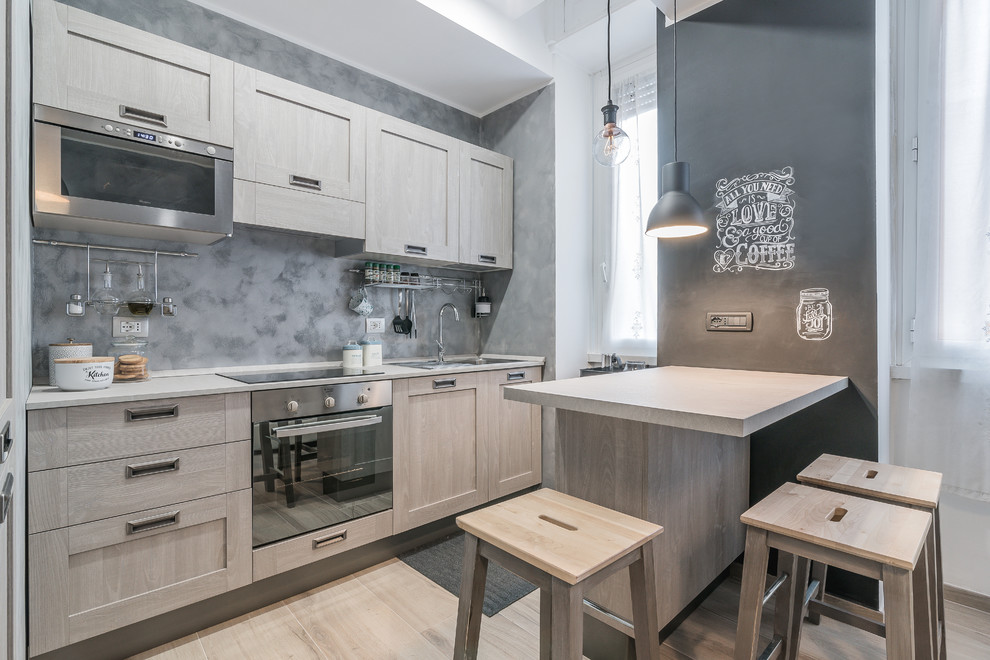 Mid-sized contemporary single-wall eat-in kitchen in Rome with a drop-in sink, recessed-panel cabinets, light wood cabinets, solid surface benchtops, grey splashback, stainless steel appliances and light hardwood floors.