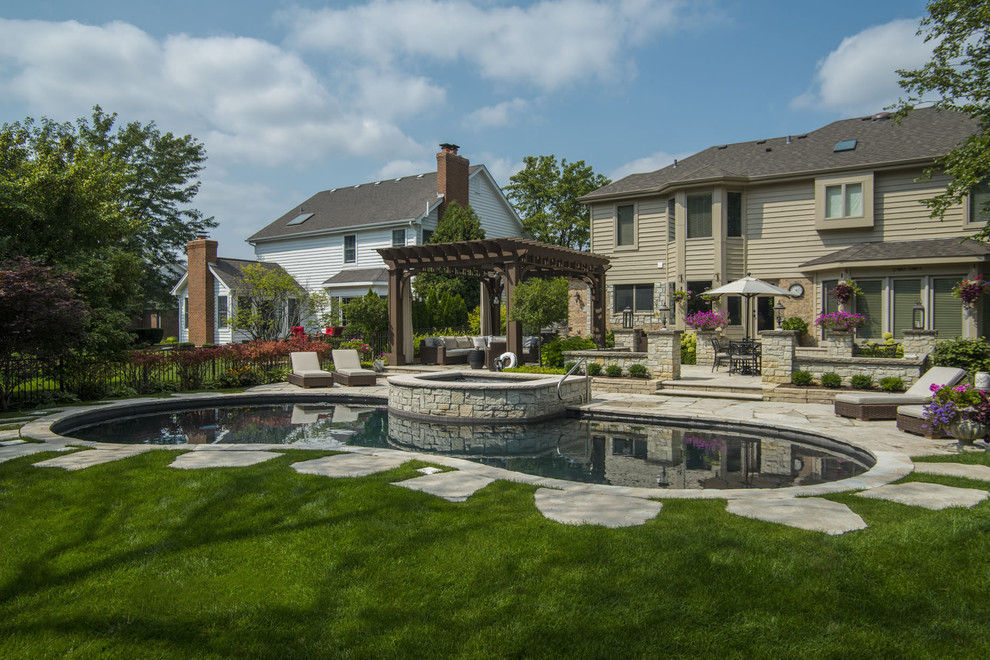 This is an example of a mid-sized arts and crafts backyard custom-shaped pool in Chicago with a hot tub and natural stone pavers.
