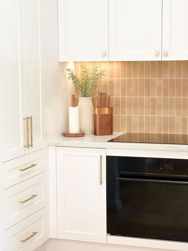Inspiration for a mid-sized beach style u-shaped kitchen pantry in Gold Coast - Tweed with an undermount sink, recessed-panel cabinets, white cabinets, quartz benchtops, pink splashback, subway tile splashback, black appliances, with island and white benchtop.
