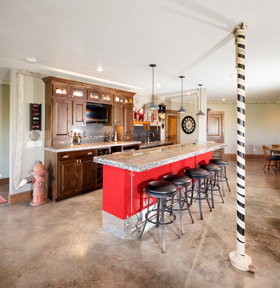 This is an example of a large transitional galley seated home bar in Other with raised-panel cabinets, medium wood cabinets, stainless steel benchtops, grey splashback, porcelain splashback, concrete floors and grey floor.