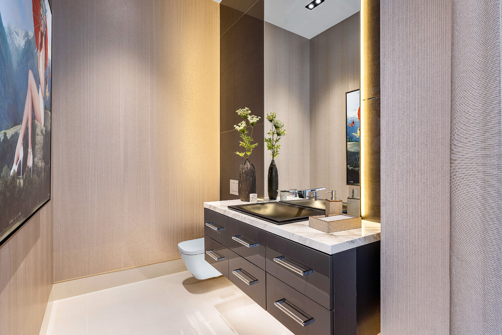 Photo of a large contemporary powder room in Miami with flat-panel cabinets, grey cabinets, a wall-mount toilet, marble floors, onyx benchtops, white floor, beige walls and white benchtops.
