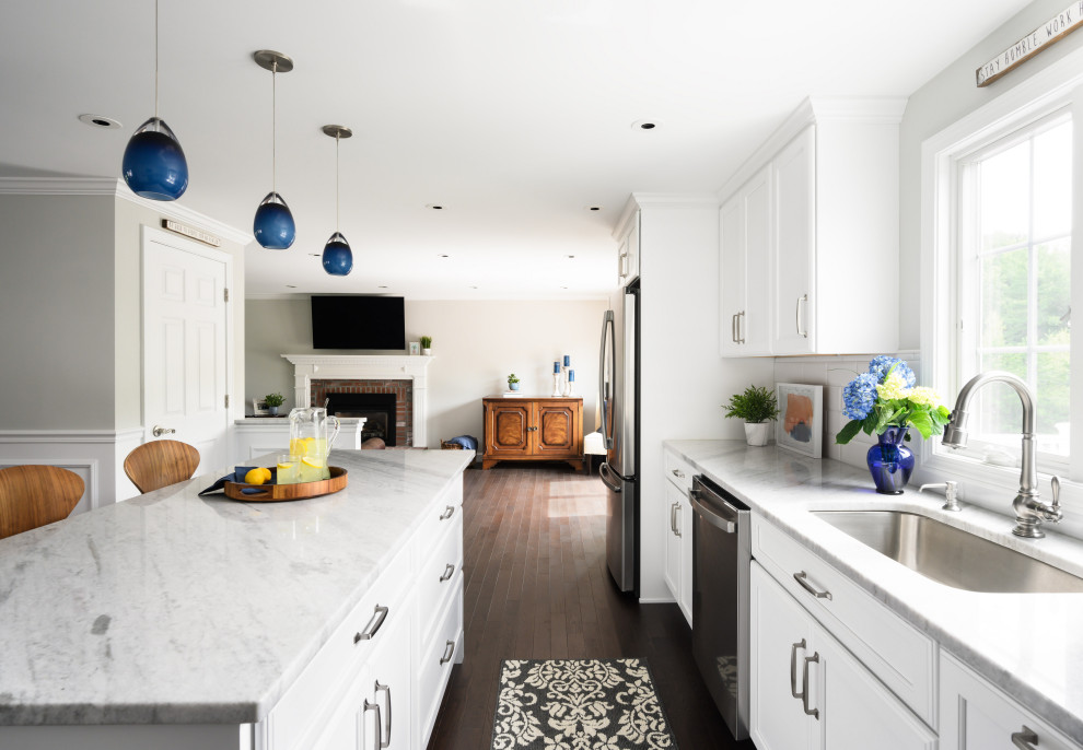 This is an example of a mid-sized traditional l-shaped eat-in kitchen in Boston with white cabinets, quartzite benchtops, white splashback, subway tile splashback, stainless steel appliances, vinyl floors, with island, brown floor and white benchtop.
