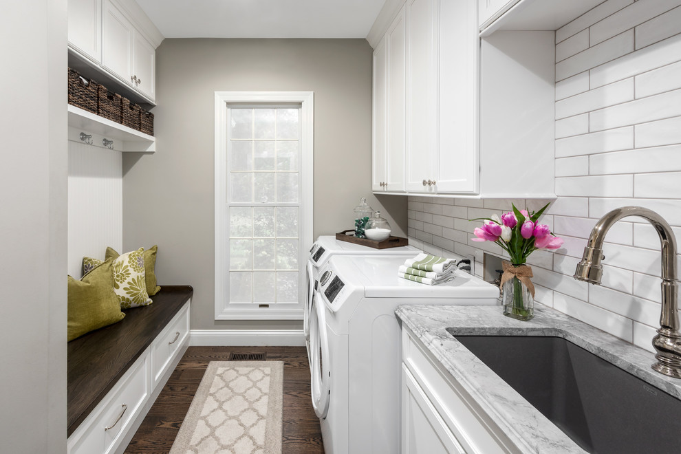 This is an example of a mid-sized traditional galley utility room in St Louis with an undermount sink, flat-panel cabinets, white cabinets, quartzite benchtops, grey walls, medium hardwood floors, a side-by-side washer and dryer, brown floor and grey benchtop.