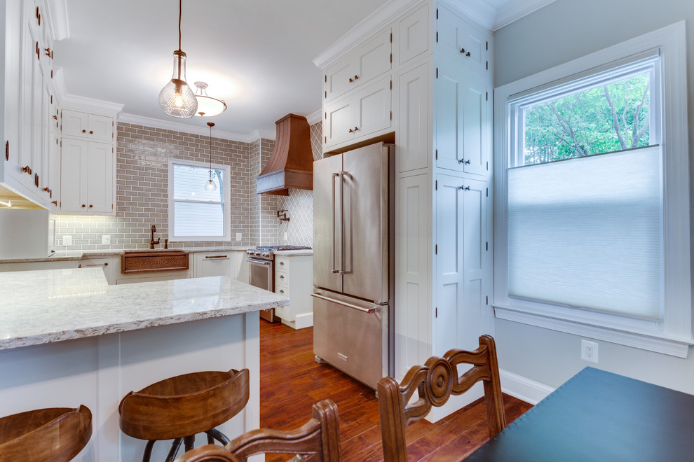 Mid-sized traditional u-shaped kitchen in DC Metro with a farmhouse sink, white cabinets, quartz benchtops, stainless steel appliances, medium hardwood floors and a peninsula.