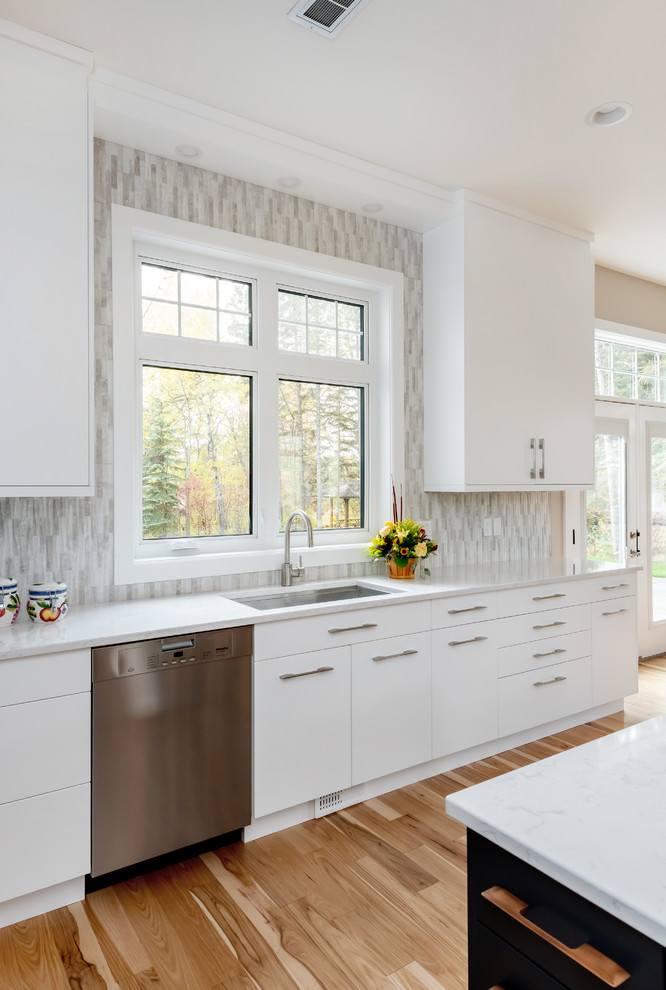 Kitchen pantry - large transitional l-shaped light wood floor and beige floor kitchen pantry idea with a double-bowl sink, flat-panel cabinets, white cabinets, quartz countertops, gray backsplash, cement tile backsplash, stainless steel appliances, an island and white countertops