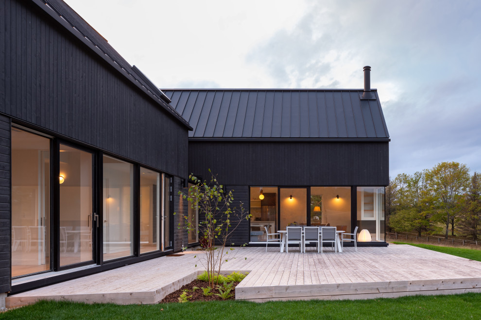 На фото: большой, двухэтажный, деревянный, черный частный загородный дом в стиле модернизм с двускатной крышей, металлической крышей и черной крышей