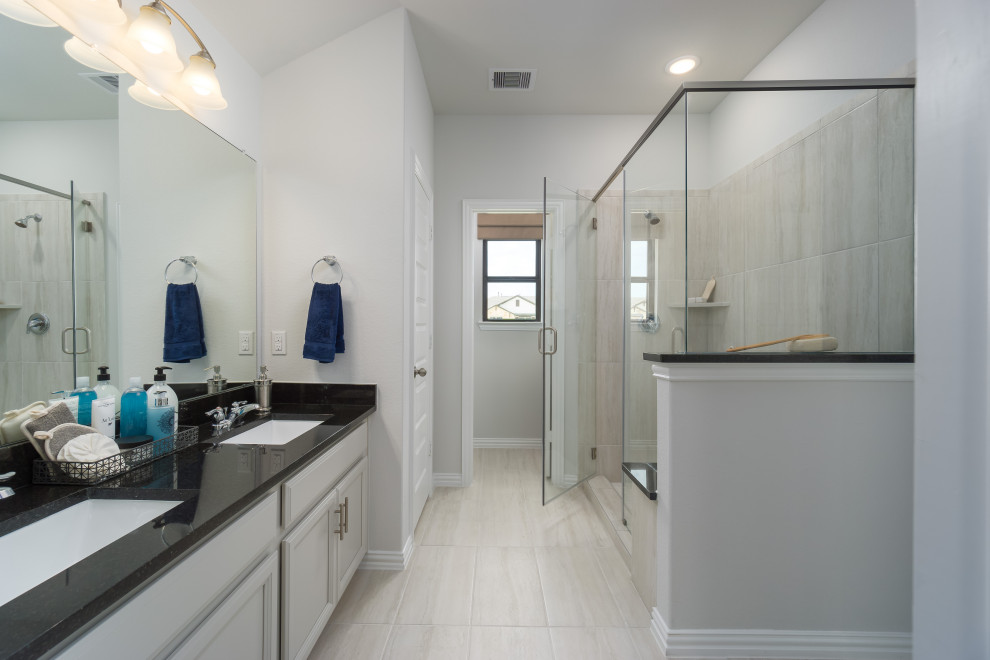 Inspiration for a mid-sized contemporary master bathroom in Houston with recessed-panel cabinets, beige cabinets, an alcove shower, beige tile, ceramic tile, beige walls, light hardwood floors, an undermount sink, solid surface benchtops, beige floor, a hinged shower door, black benchtops and a double vanity.