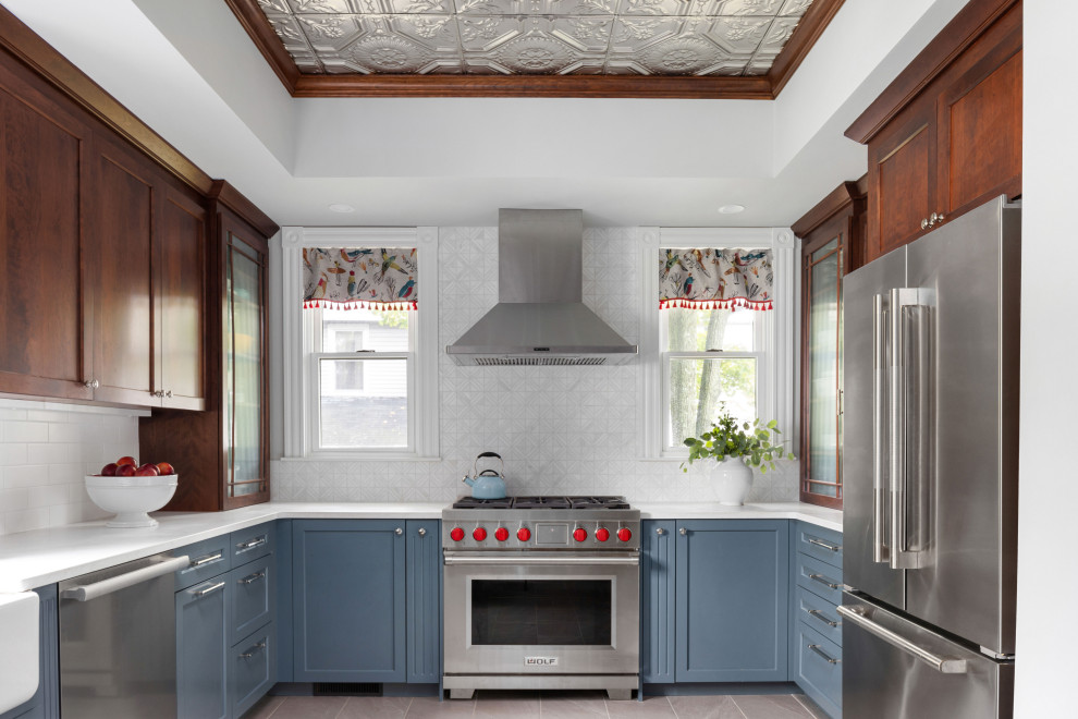 Victorian u-shaped kitchen in Boston with a belfast sink, shaker cabinets, blue cabinets, engineered stone countertops, grey splashback, mosaic tiled splashback, stainless steel appliances, porcelain flooring, a breakfast bar, grey floors, white worktops and a drop ceiling.