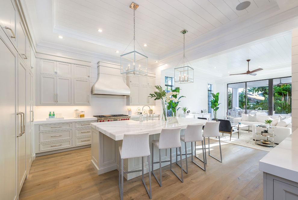 Design ideas for a beach style l-shaped kitchen in Miami with a farmhouse sink, recessed-panel cabinets, grey cabinets, stainless steel appliances, medium hardwood floors, with island, brown floor and white benchtop.