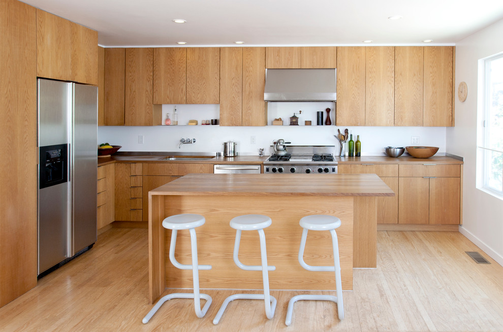 Photo of a modern l-shaped kitchen in San Francisco with an undermount sink, flat-panel cabinets, medium wood cabinets, wood benchtops, stainless steel appliances, light hardwood floors and with island.