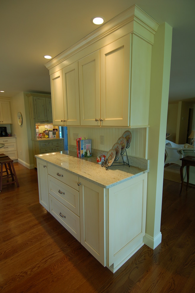 Design ideas for a mid-sized beach style eat-in kitchen in Boston with a farmhouse sink, recessed-panel cabinets, yellow cabinets, granite benchtops, white splashback, panelled appliances, medium hardwood floors and with island.