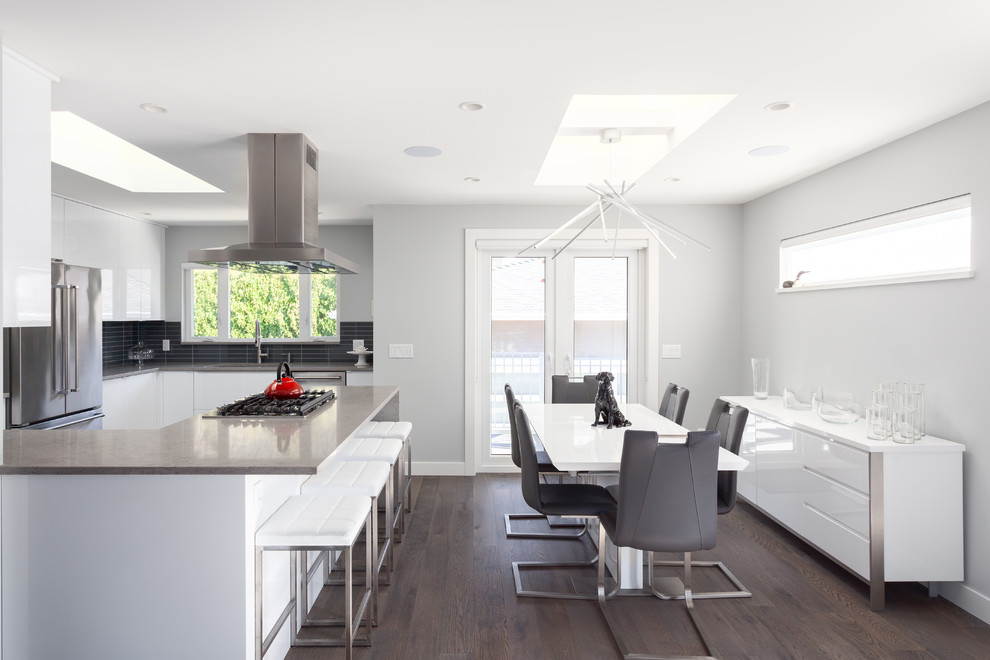 Photo of a mid-sized modern u-shaped open plan kitchen in Vancouver with an undermount sink, flat-panel cabinets, white cabinets, quartz benchtops, black splashback, porcelain splashback, stainless steel appliances, dark hardwood floors, with island, brown floor and grey benchtop.