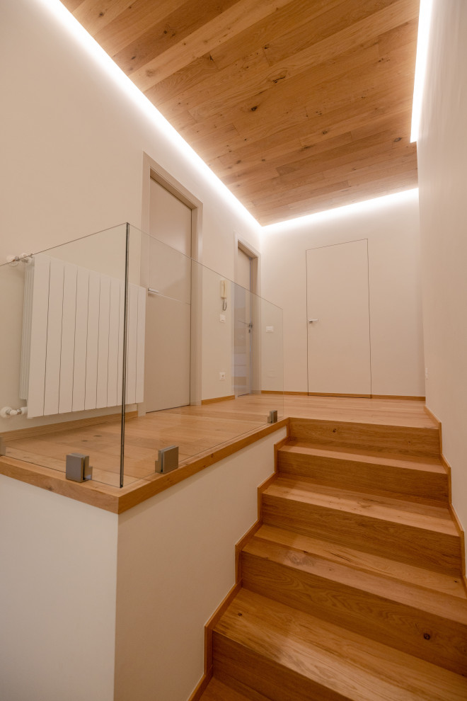 Small danish wooden l-shaped glass railing staircase photo in Milan with wooden risers