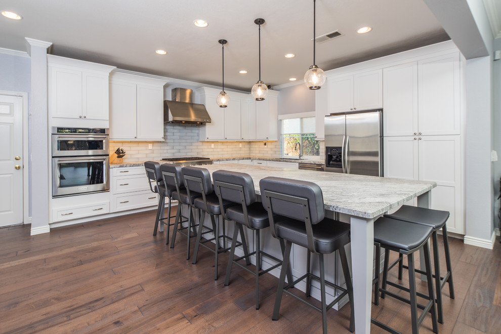 Photo of a large modern l-shaped kitchen in San Diego with an undermount sink, stainless steel appliances, dark hardwood floors, brown floor, grey splashback, glass tile splashback, shaker cabinets, white cabinets, granite benchtops and with island.