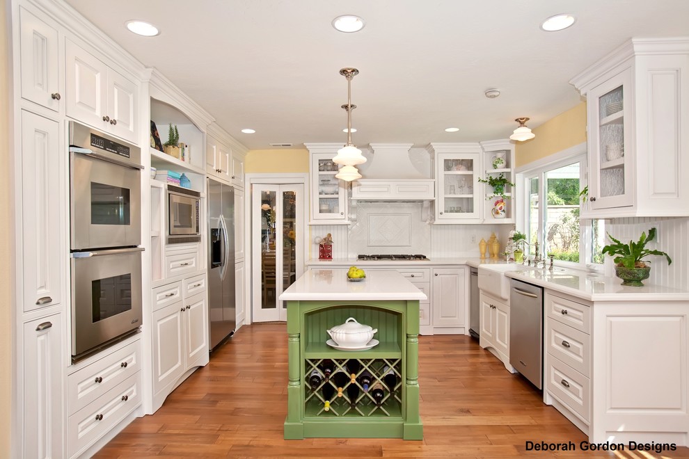 Photo of a mid-sized traditional u-shaped open plan kitchen in San Diego with a farmhouse sink, shaker cabinets, white cabinets, stainless steel appliances, medium hardwood floors and with island.