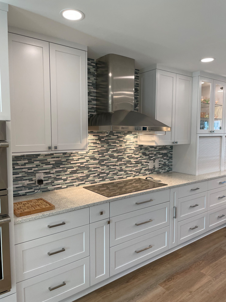 Large beach style galley eat-in kitchen in Raleigh with an undermount sink, recessed-panel cabinets, white cabinets, quartzite benchtops, blue splashback, glass tile splashback, stainless steel appliances, vinyl floors, a peninsula, brown floor and turquoise benchtop.