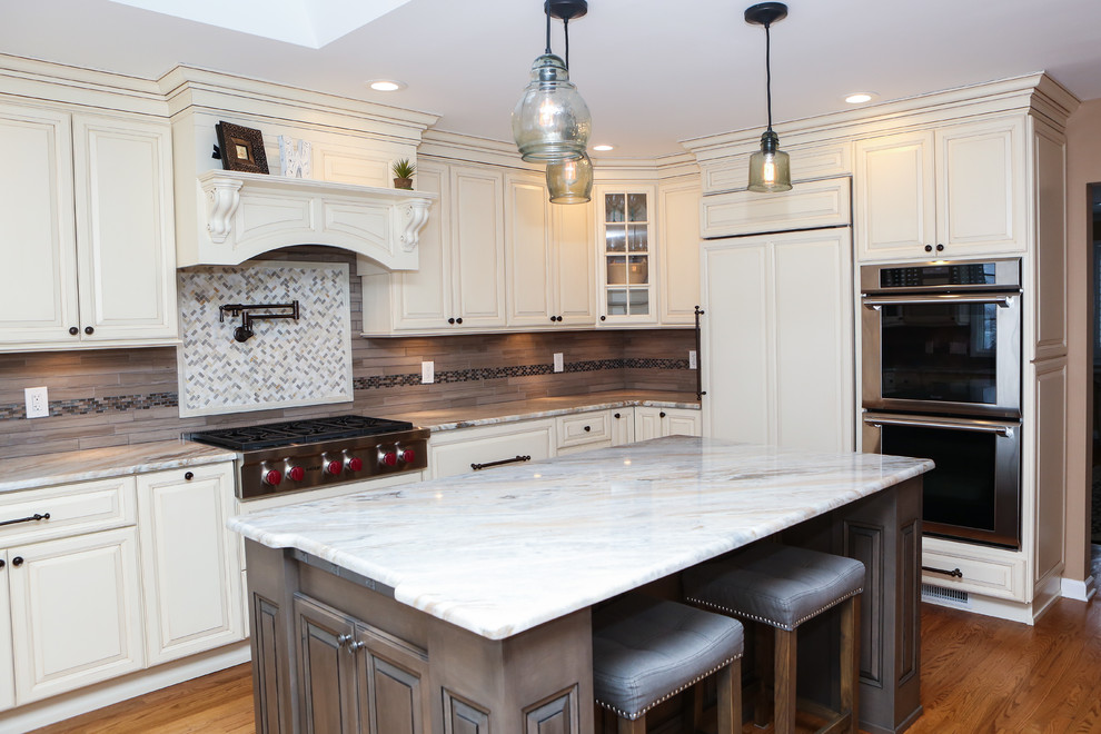 Inspiration for a large transitional u-shaped light wood floor eat-in kitchen remodel in Newark with an undermount sink, raised-panel cabinets, distressed cabinets, granite countertops, brown backsplash, mosaic tile backsplash, stainless steel appliances and an island