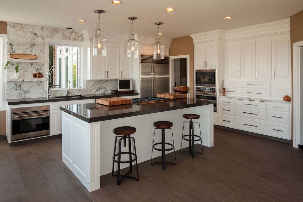 Large transitional dark wood floor kitchen photo with a drop-in sink, raised-panel cabinets, white cabinets, quartzite countertops, stone slab backsplash, stainless steel appliances and an island