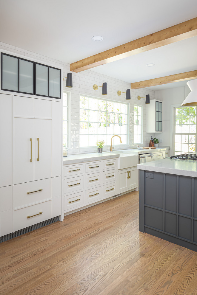 Design ideas for a mid-sized country single-wall open plan kitchen in Raleigh with a farmhouse sink, flat-panel cabinets, white cabinets, quartzite benchtops, white splashback, subway tile splashback, panelled appliances, light hardwood floors, with island and white benchtop.