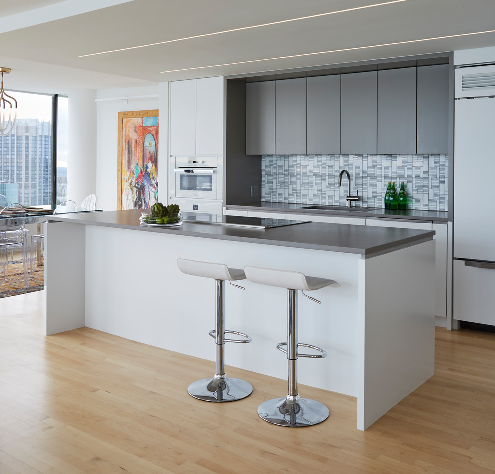 Small modern galley open plan kitchen in Chicago with an undermount sink, flat-panel cabinets, white cabinets, quartz benchtops, white splashback, glass tile splashback, panelled appliances, light hardwood floors and with island.