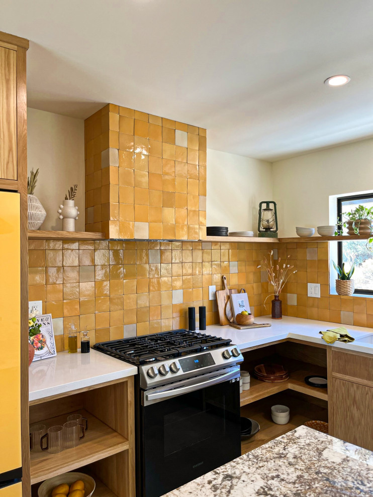 Inredning av ett amerikanskt vit vitt kök, med en undermonterad diskho, släta luckor, skåp i mellenmörkt trä, bänkskiva i kvarts, gult stänkskydd, stänkskydd i terrakottakakel, rostfria vitvaror, betonggolv, en köksö och grått golv