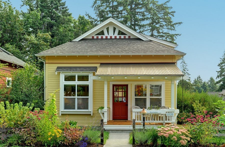 This is an example of a small arts and crafts two-storey yellow house exterior in Other with concrete fiberboard siding, a hip roof and a shingle roof.