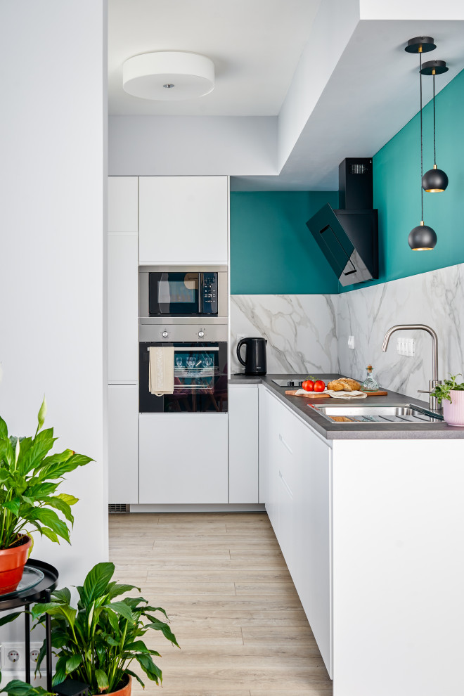 Scandinavian l-shaped kitchen in Saint Petersburg with an undermount sink, flat-panel cabinets, white cabinets, white splashback, stone slab splashback, stainless steel appliances, light hardwood floors, beige floor and grey benchtop.