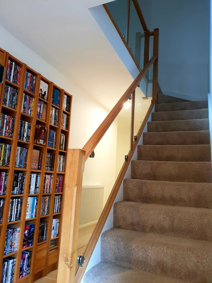 Mid-sized carpeted l-shaped staircase in Other with carpet risers and wood railing.