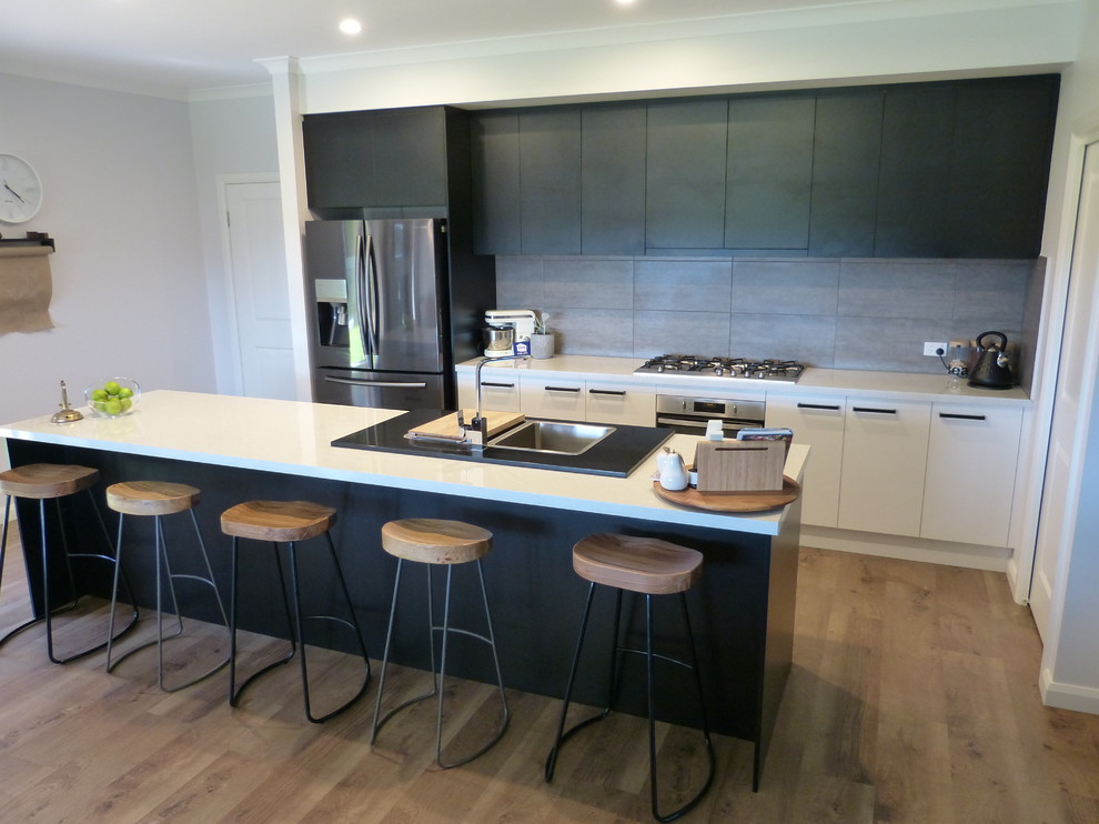 Inspiration for a large contemporary galley open plan kitchen in Adelaide with a double-bowl sink, flat-panel cabinets, black cabinets, laminate benchtops, grey splashback, cement tile splashback, stainless steel appliances, laminate floors, with island, brown floor and white benchtop.