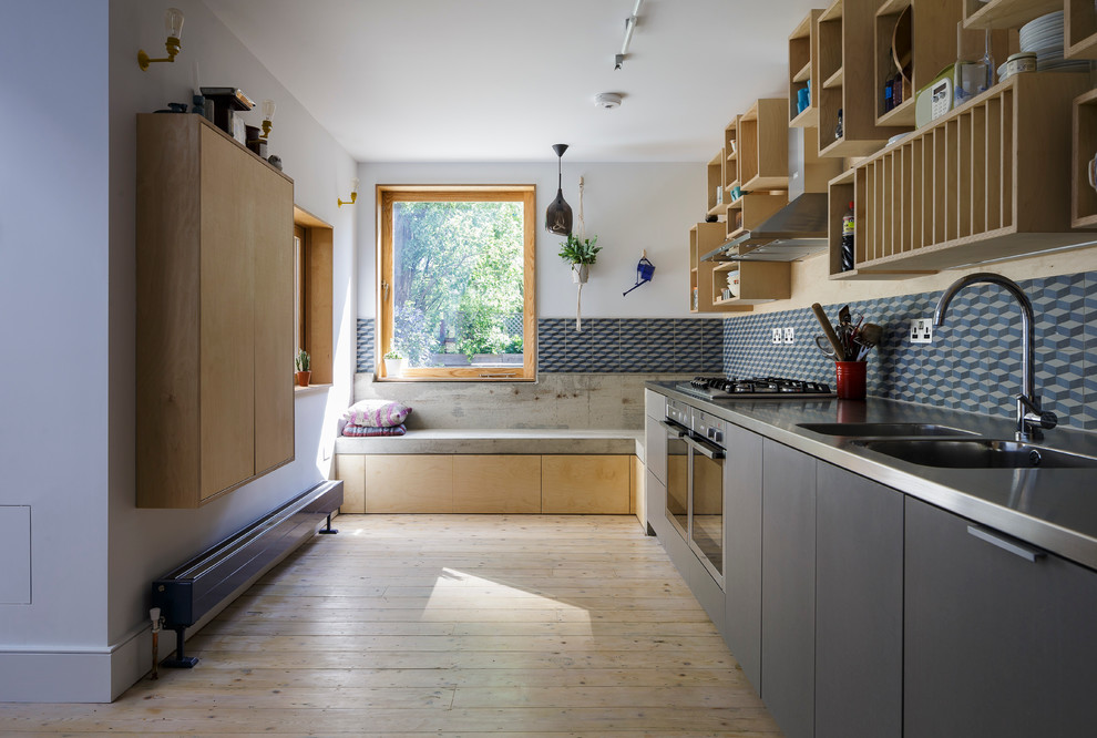 This is an example of a mid-sized contemporary l-shaped open plan kitchen in London with a double-bowl sink, flat-panel cabinets, light wood cabinets, stainless steel benchtops, multi-coloured splashback, ceramic splashback, stainless steel appliances, light hardwood floors and no island.