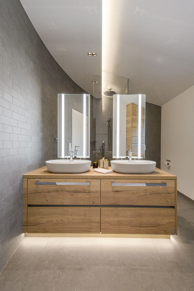 Idéer för industriella brunt en-suite badrum, med en kantlös dusch, en toalettstol med separat cisternkåpa, grå kakel, keramikplattor, grå väggar, klinkergolv i keramik, träbänkskiva, grått golv och med dusch som är öppen
