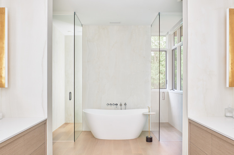 Large contemporary master bathroom in Toronto with flat-panel cabinets, beige cabinets, a freestanding tub, a curbless shower, white tile, stone slab, white walls, light hardwood floors, an undermount sink, marble benchtops, beige floor, a hinged shower door and white benchtops.