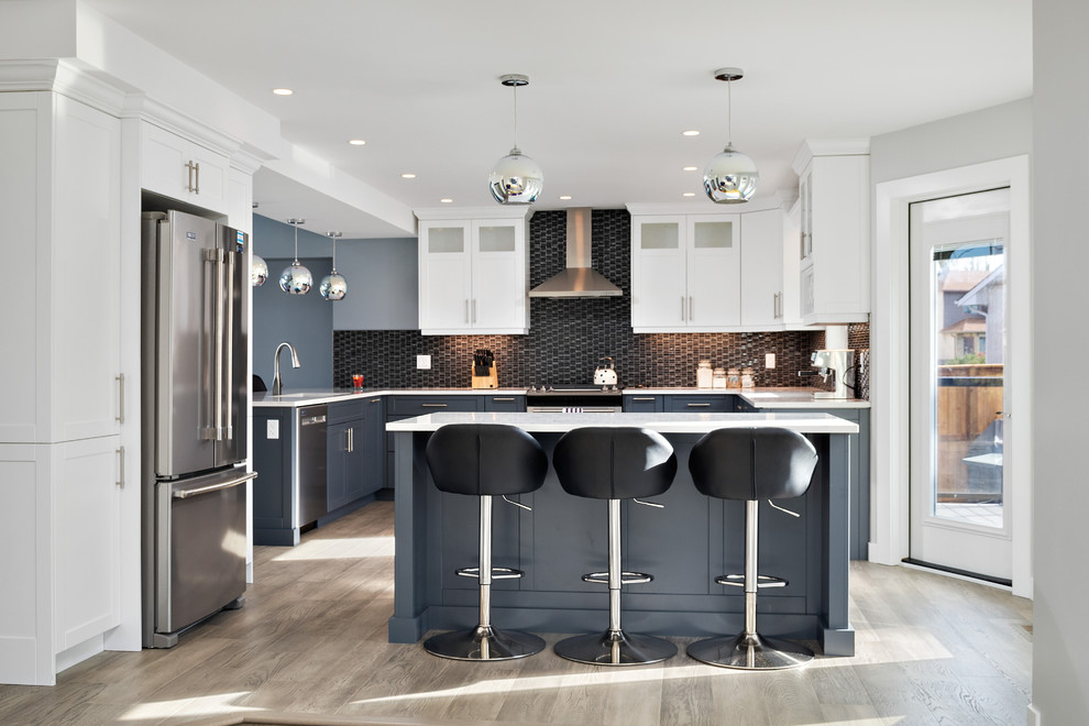 Large transitional u-shaped eat-in kitchen in Other with shaker cabinets, quartz benchtops, black splashback, glass tile splashback, stainless steel appliances, with island, white benchtop, an undermount sink, blue cabinets, medium hardwood floors and grey floor.