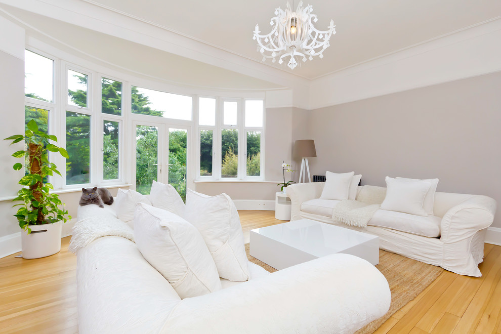 Contemporary living room in Sussex with grey walls, light hardwood floors and no fireplace.