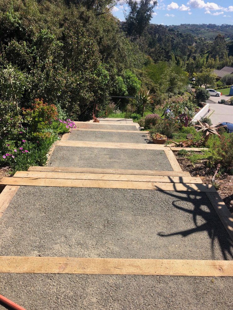 This is an example of an expansive tropical backyard full sun xeriscape for summer in San Diego with with rock feature, decomposed granite and a wood fence.