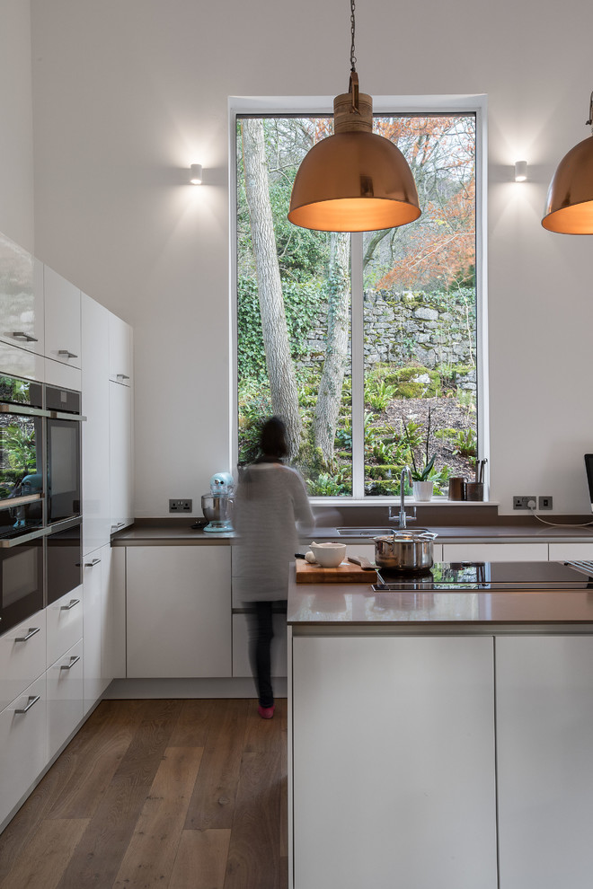 Large contemporary l-shaped eat-in kitchen in Other with flat-panel cabinets, white cabinets, solid surface benchtops, panelled appliances, medium hardwood floors, with island, brown floor, brown splashback and brown benchtop.