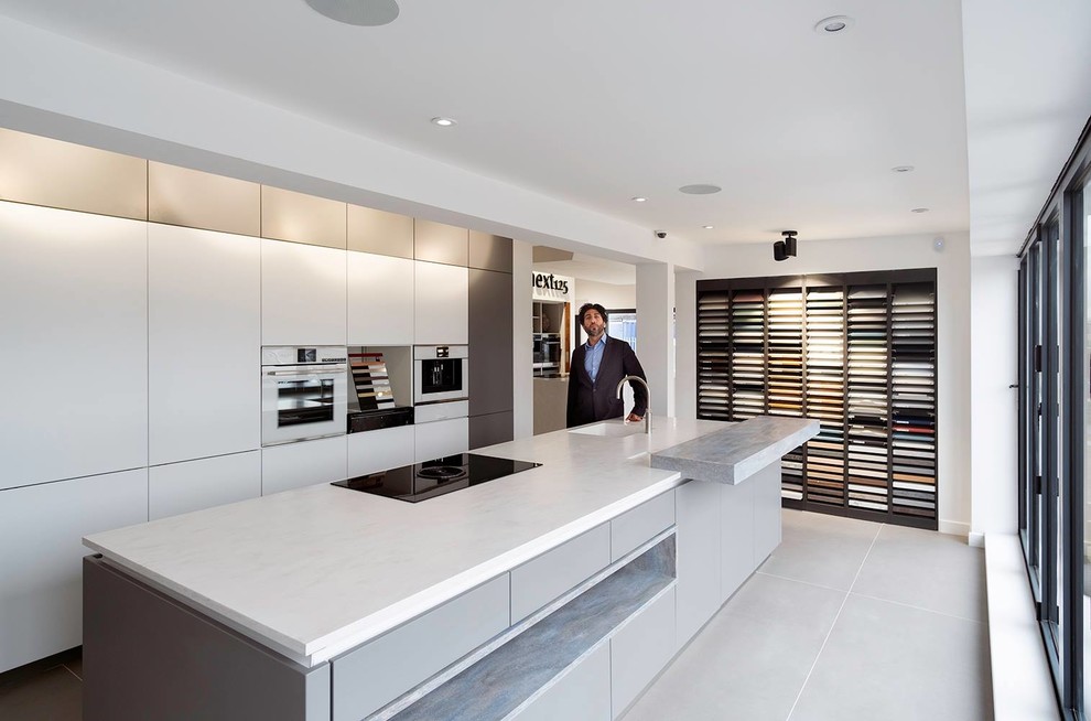 Inspiration for a large modern single-wall open plan kitchen in Other with an integrated sink, flat-panel cabinets, white cabinets, solid surface benchtops, stainless steel appliances, concrete floors, with island, grey floor and white benchtop.
