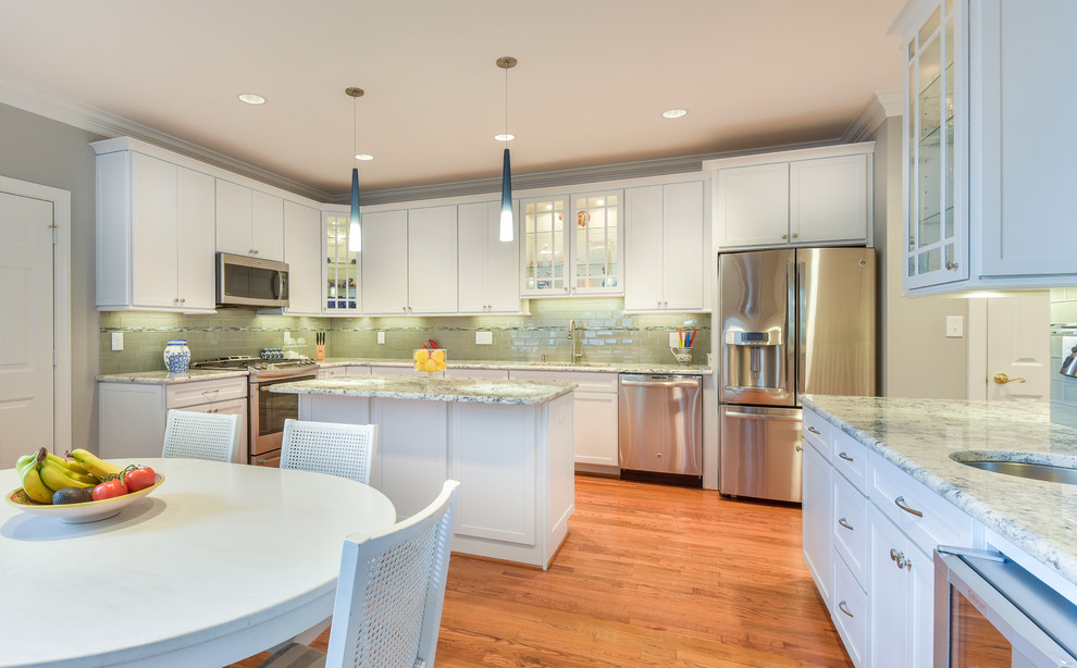 Photo of a large transitional u-shaped eat-in kitchen in DC Metro with an undermount sink, shaker cabinets, white cabinets, granite benchtops, grey splashback, glass tile splashback, stainless steel appliances, with island, medium hardwood floors and brown floor.