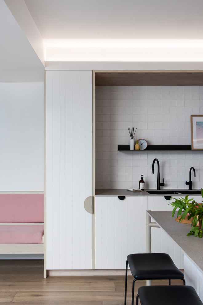 Inspiration for a mid-sized contemporary l-shaped open plan kitchen in Sydney with a double-bowl sink, white cabinets, recycled glass benchtops, white splashback, cement tile splashback, black appliances, medium hardwood floors, with island and grey benchtop.