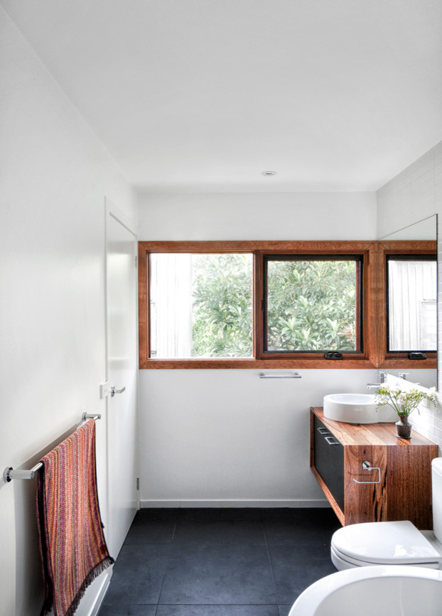 Photo of a contemporary bathroom in Melbourne with a vessel sink, flat-panel cabinets, medium wood cabinets, wood benchtops, a freestanding tub, an open shower, a one-piece toilet, white tile, ceramic tile, white walls and ceramic floors.