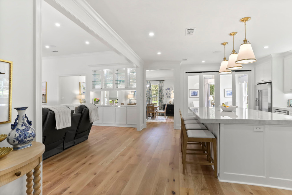 Example of a large transitional l-shaped light wood floor and brown floor open concept kitchen design in New Orleans with an undermount sink, shaker cabinets, white cabinets, quartz countertops, white backsplash, quartz backsplash, stainless steel appliances, an island and white countertops
