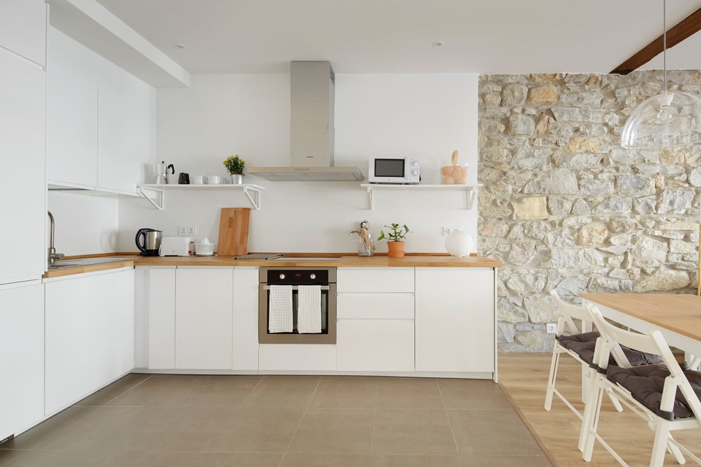 Inspiration for a mediterranean l-shaped open plan kitchen in Other with a drop-in sink, flat-panel cabinets, white cabinets, wood benchtops, white splashback, no island, grey floor and beige benchtop.