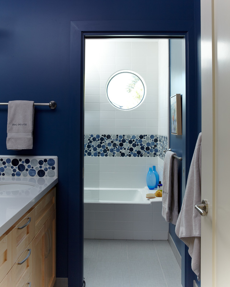 This is an example of a small beach style bathroom in San Francisco with an undermount sink, recessed-panel cabinets, light wood cabinets, a two-piece toilet, blue tile, glass tile, blue walls and porcelain floors.