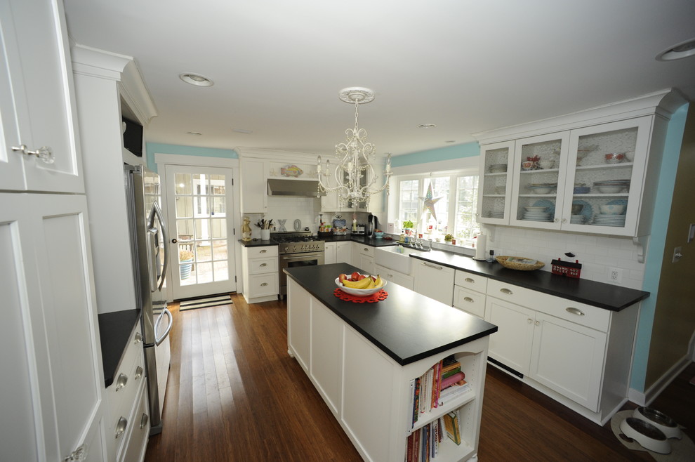 Example of a large transitional u-shaped medium tone wood floor enclosed kitchen design in Baltimore with a farmhouse sink, glass-front cabinets, white cabinets, soapstone countertops, white backsplash, subway tile backsplash, stainless steel appliances and an island