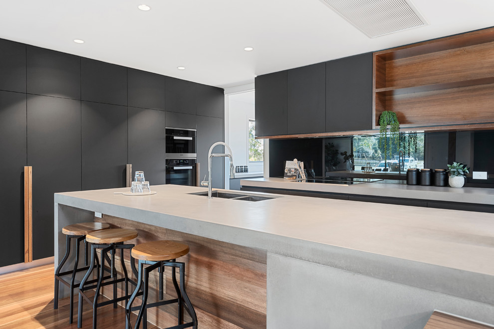 This is an example of a large industrial galley eat-in kitchen in Brisbane with mirror splashback, medium hardwood floors, with island, grey benchtop, a double-bowl sink, flat-panel cabinets, grey cabinets and brown floor.