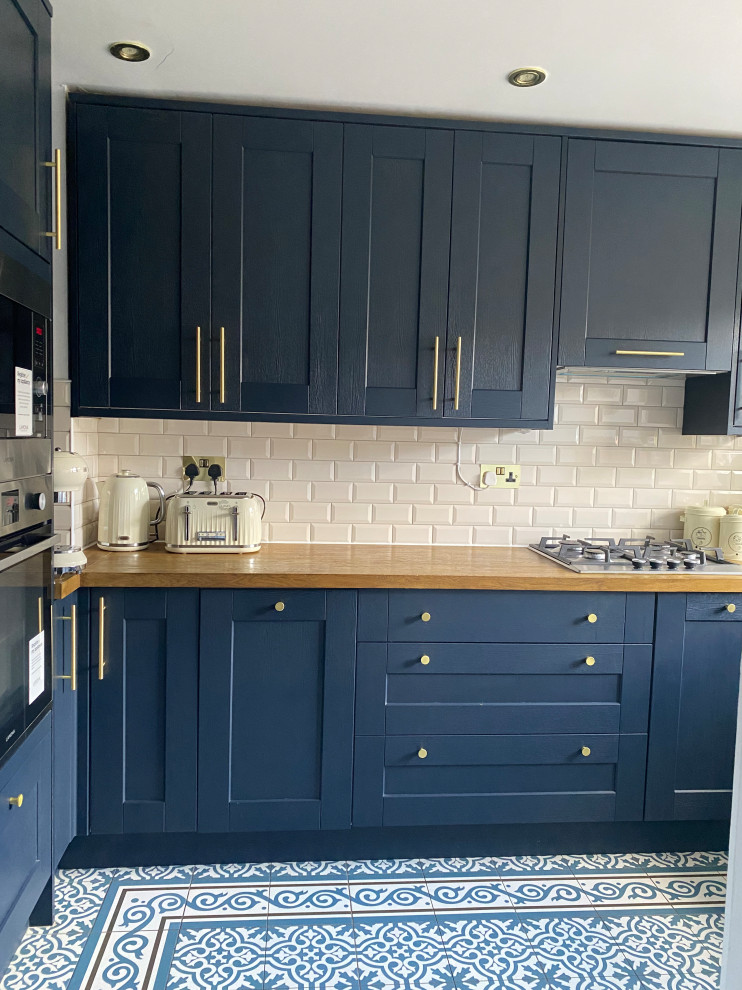 Inspiration for a mid-sized contemporary u-shaped separate kitchen in London with a farmhouse sink, blue cabinets, wood benchtops, white splashback, ceramic splashback, porcelain floors, no island, blue floor and coffered.
