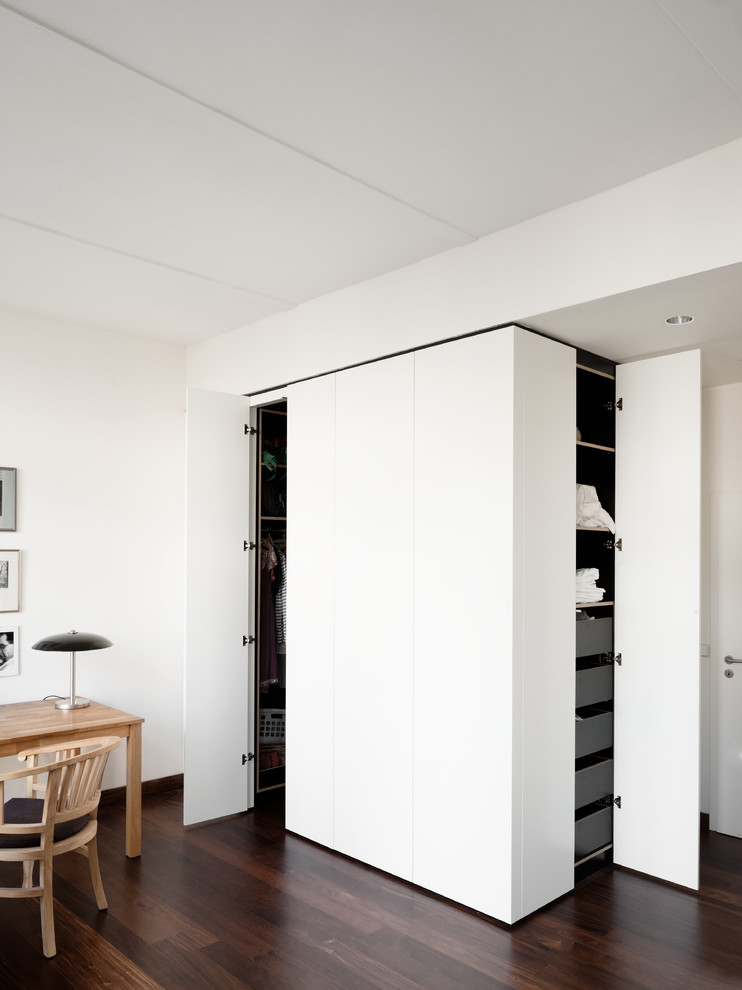 Inspiration for a small contemporary gender-neutral walk-in wardrobe in Berlin with flat-panel cabinets, white cabinets and dark hardwood floors.